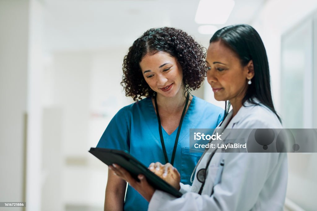 Cheerful female nurse with curly hair looking at digital tablet held by female doctor smiling together in hospital